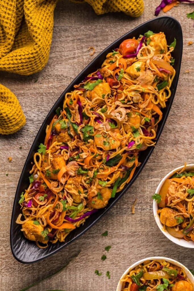 Noodles on a boat shaped bowl with chicken, shrimp, and vegetables served in a homemade curry sauce. 