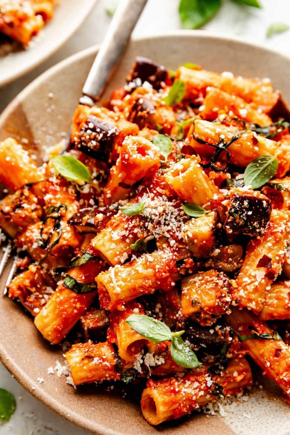 Pasta with roast eggplant and sauce sprinkled with parmesan cheese served on a brown plate. 