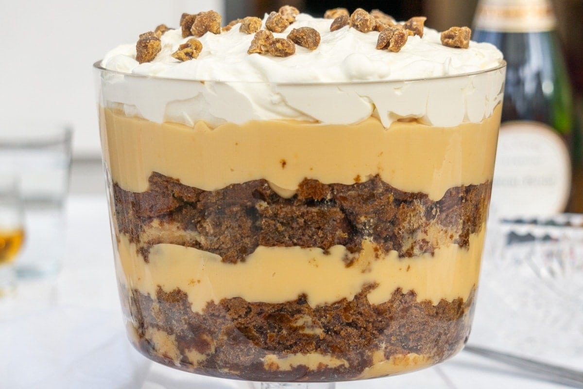 Sticky toffee pudding trifle made with layers of chocolate sponge cake, fruit, custard, and cream. topped with whipped cream and chopped nuts.  