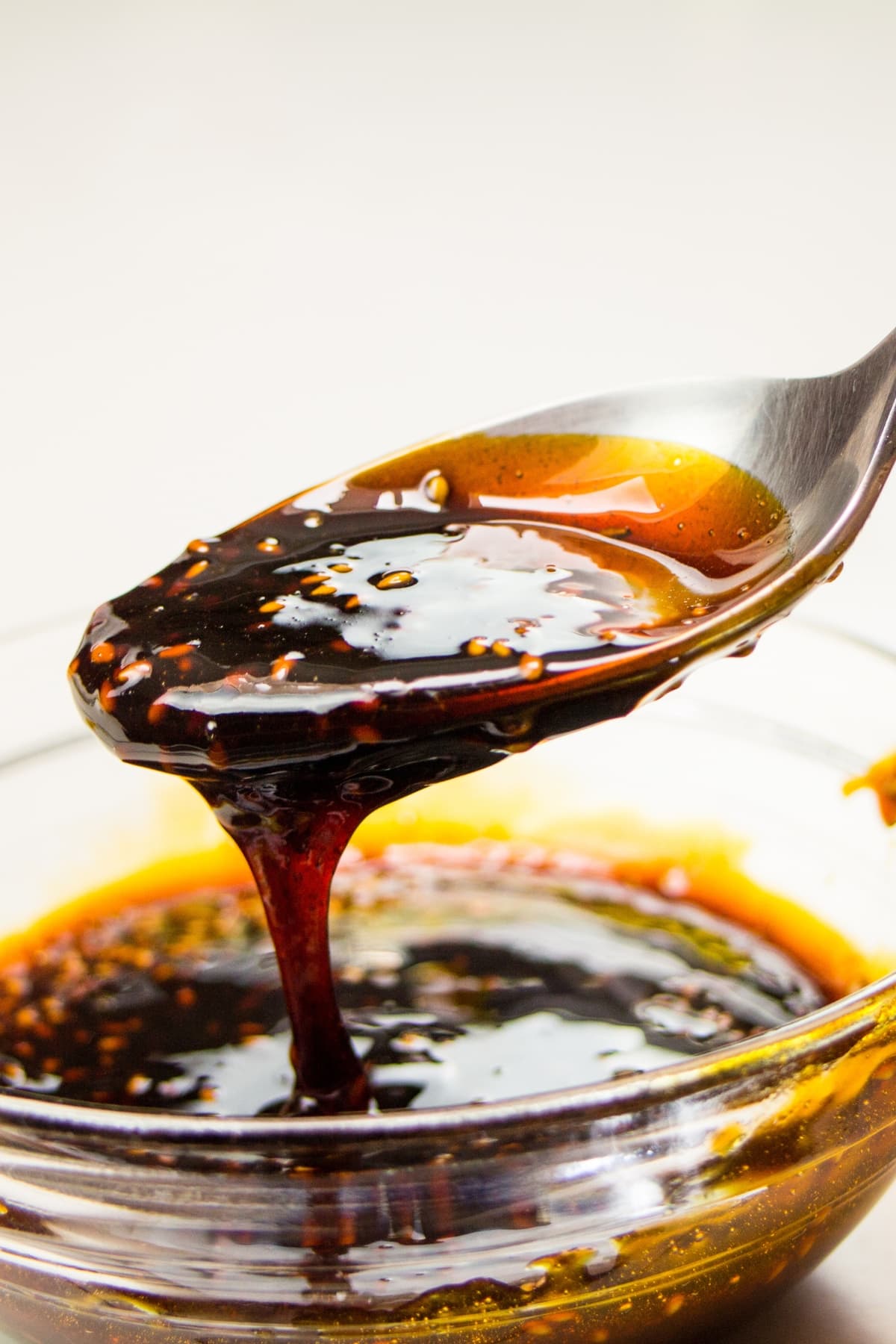 A person holding a spoon in a container of teriyaki sauce