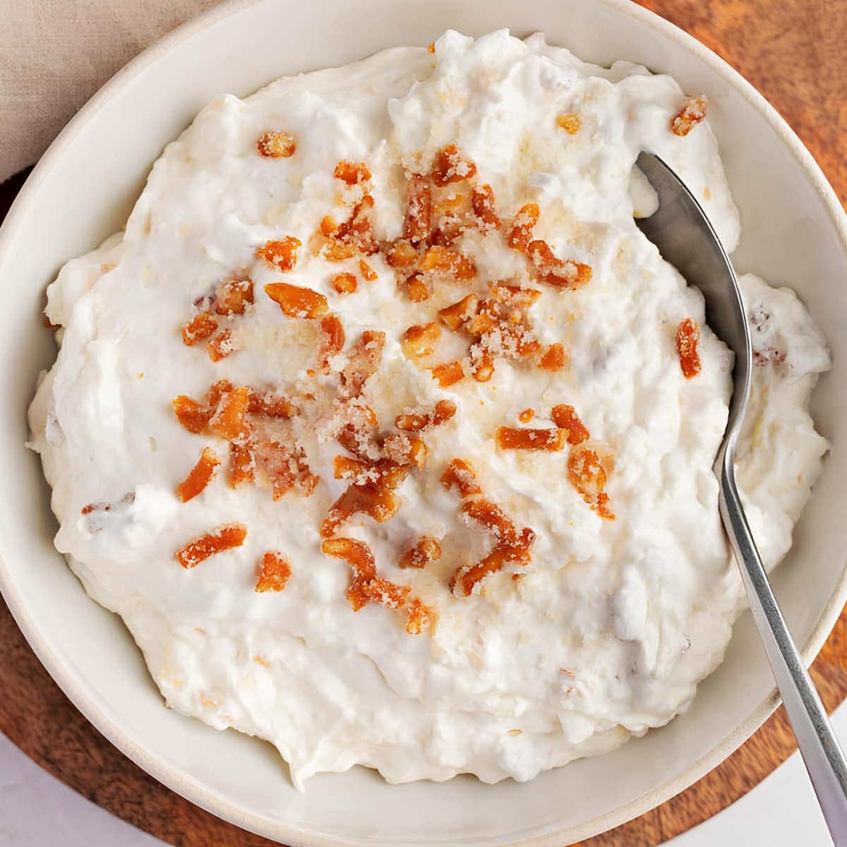 Top view of pineapple pretzel fluff with crushed pretzels on top in a bowl with a spoon. 