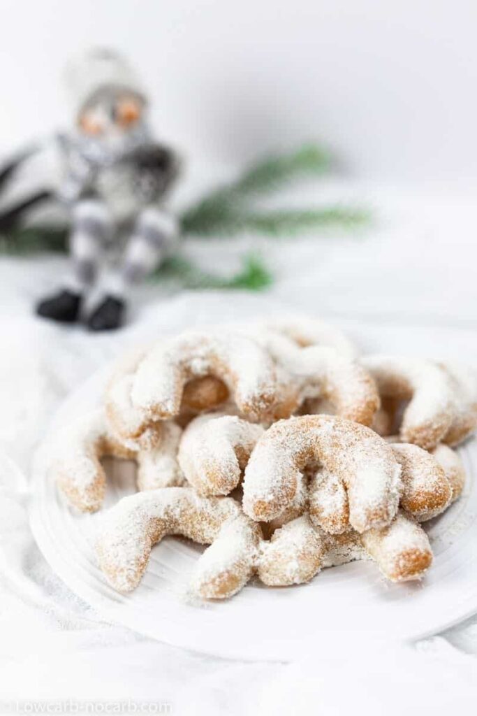 Bunch of crescent shaped cookies on a cake covered with powdered sugar. 