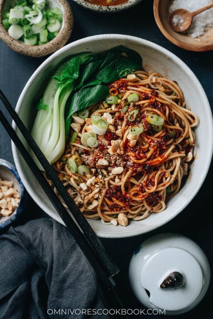 A plate of Chinese noodles with bok choy, chopped onion leaves and peanut in peanut sauce. 