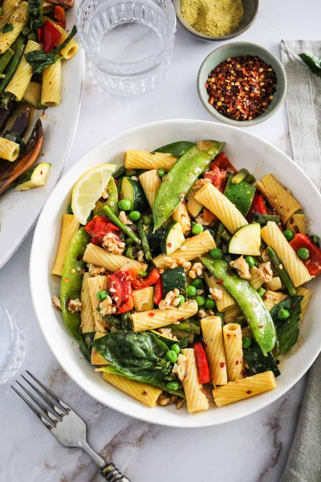 Pasta with asparagus, peas, red bell pepper, zucchini, and cherry tomatoes served on a white bowl. 