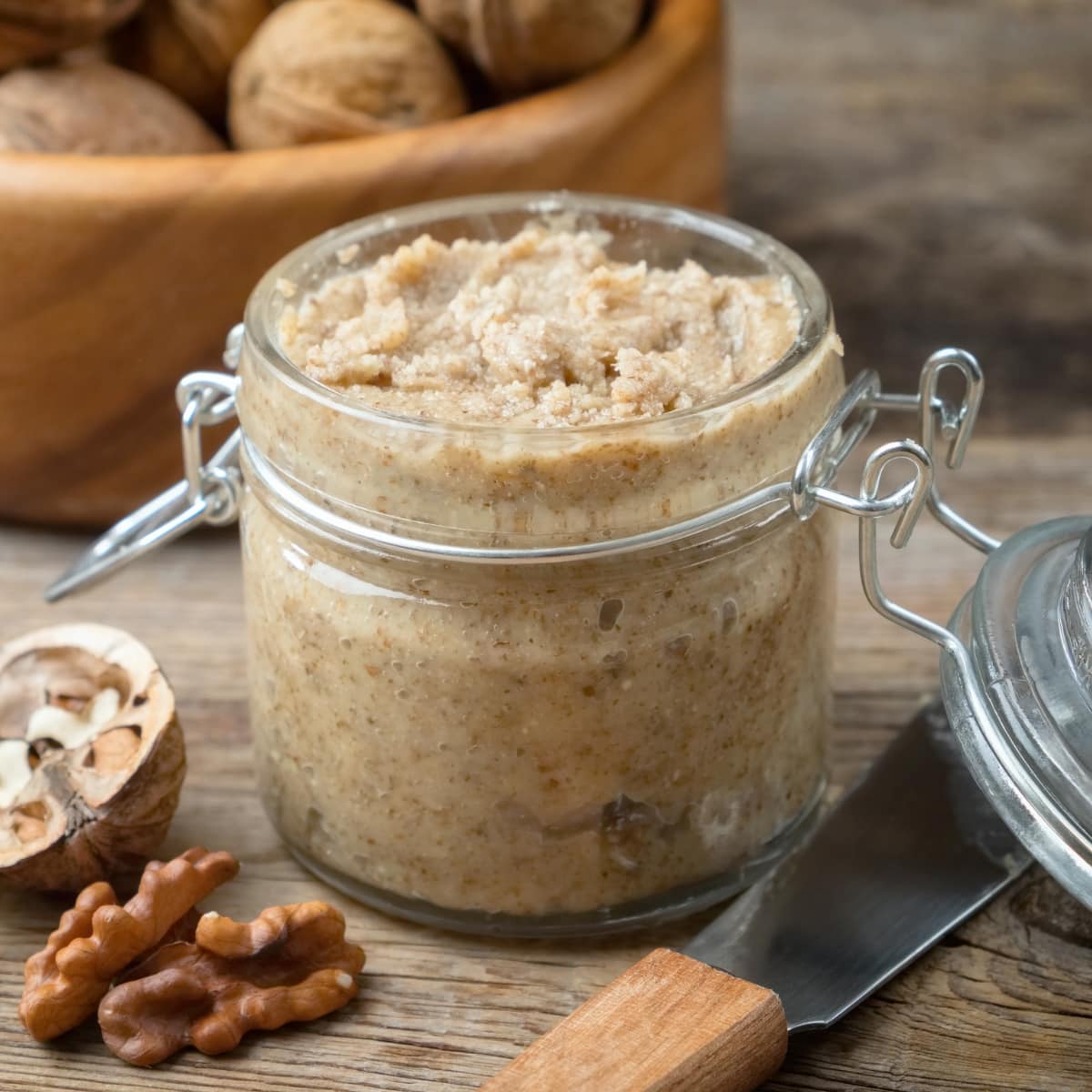Walnut Butter in a Glass Jar with Nuts on a Wooden Board