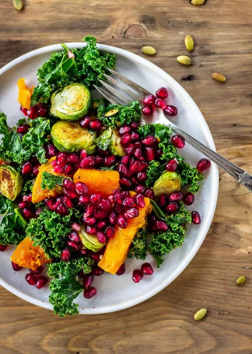 Salad on a white plate made with crispy Brussels sprouts, roasted butternut squash, and fresh pomegranate.