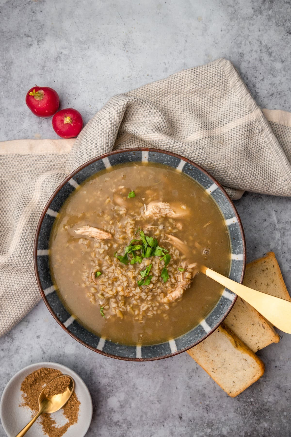 Freekeh soup combined with chicken and spices in a bowl, with a spoon and served with bread- top view