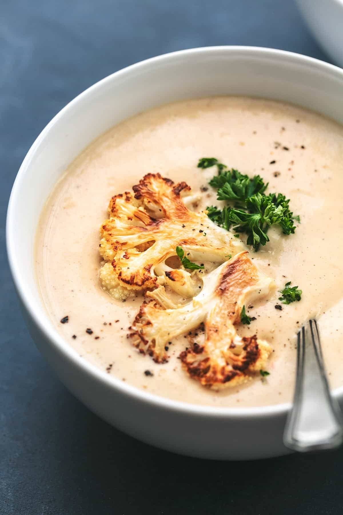 Bowl of creamy roasted cauliflower soup with chunks of roasted cauliflower, parsley, and black pepper in a bowl with a spoon