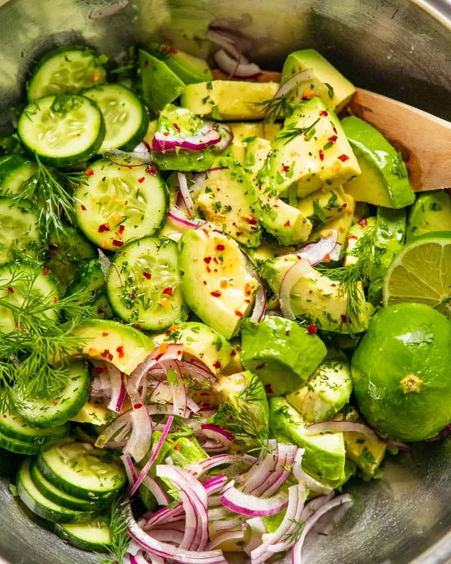 Ripe avocado tossed with olive oil, onion, cilantro, dill, cucumber and lime on a mixing bowl.