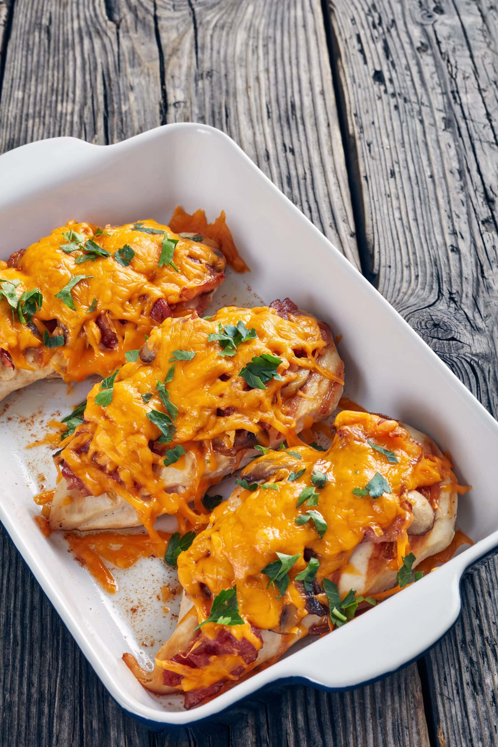 Baked chicken breast on a dish topped with honey mustard sauce, bacon and sauteed mushroom. 