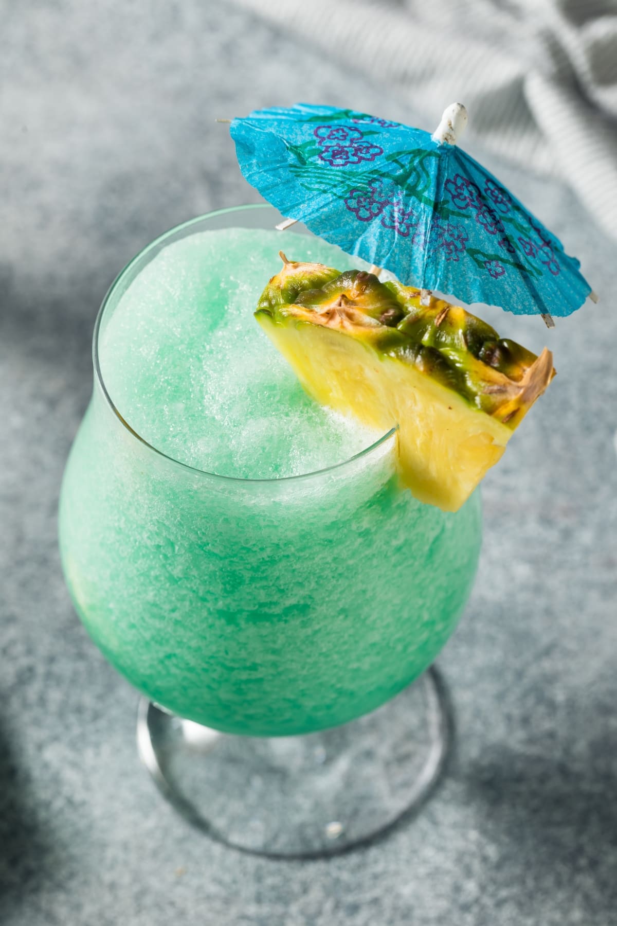 Blue Hawaiian cocktail garnished with cocktail umbrella and pineapple slices. 
