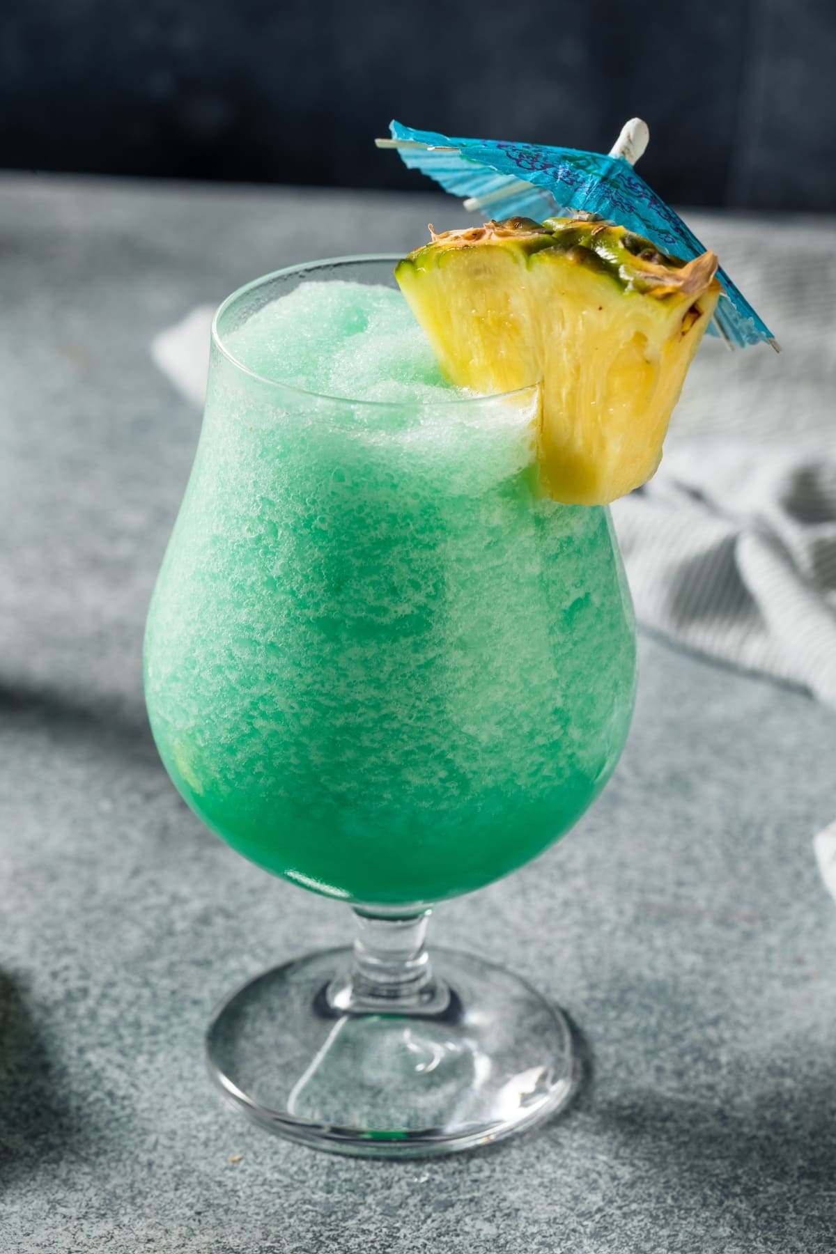 Blue Hawaiian Cocktail in a glass garnished with pineapple slice and blue paper umbrella.