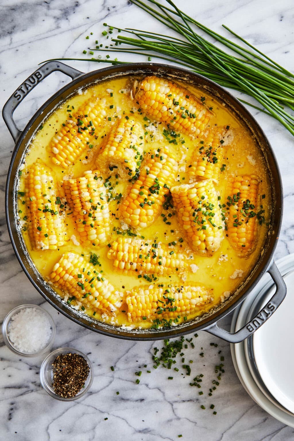 Corn on the cob soaked in butter sauce in a cast iron pan sprinkled with chopped onion leaves.