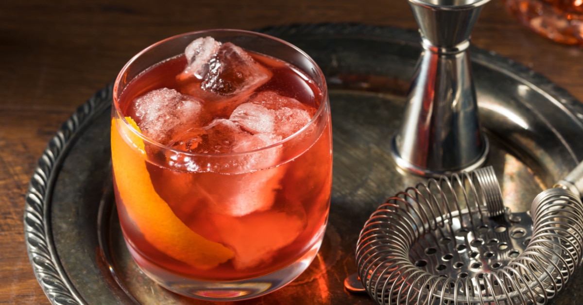 Boulevardier cocktail, mixer and strainer on a steel tray.