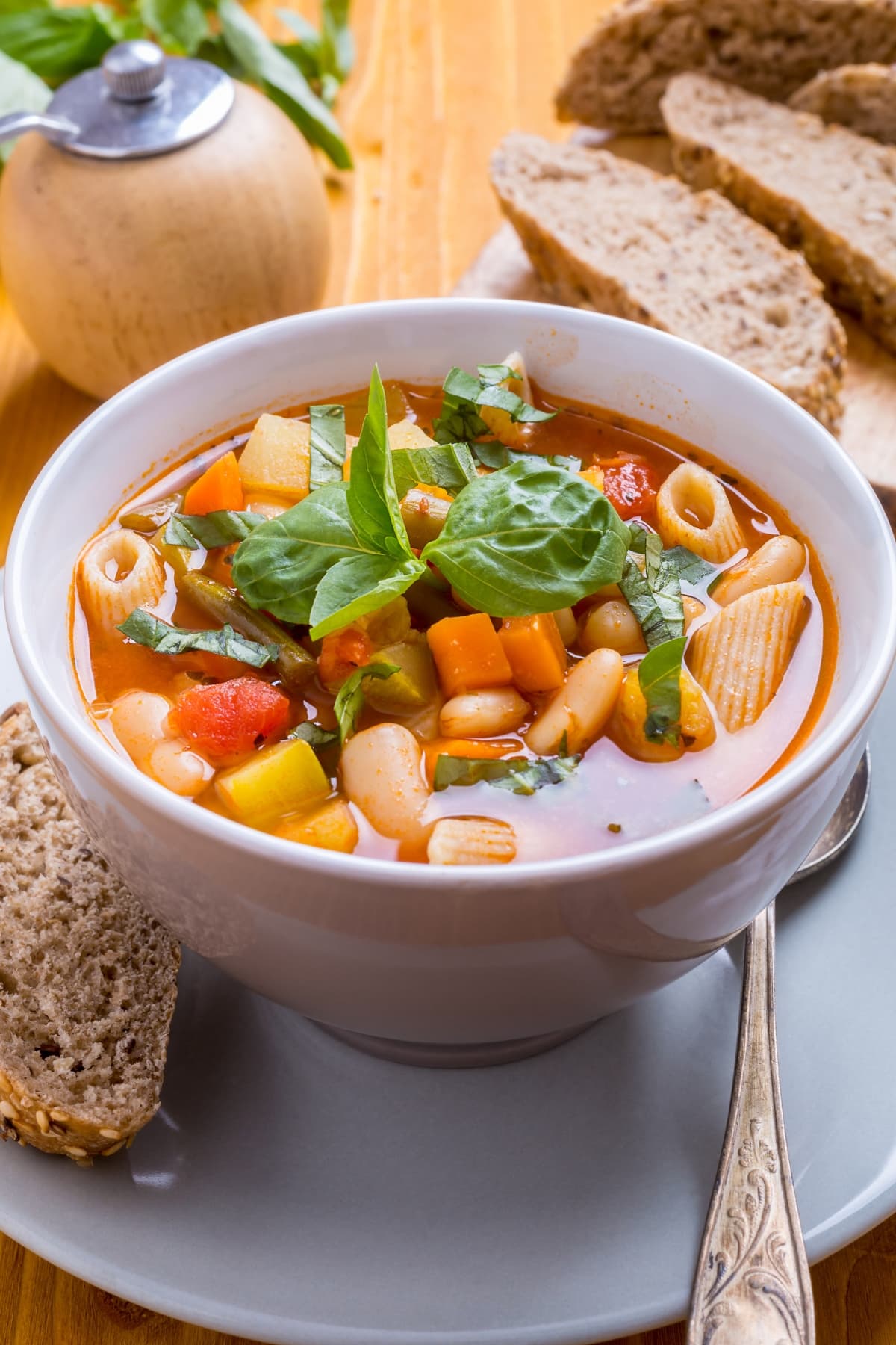 25 Soups That Freeze Well (+ Easy Recipes!) featuring bowl of homemade minestrone soup with beans, pasta, tomatoes and carrots, plus bread on the side