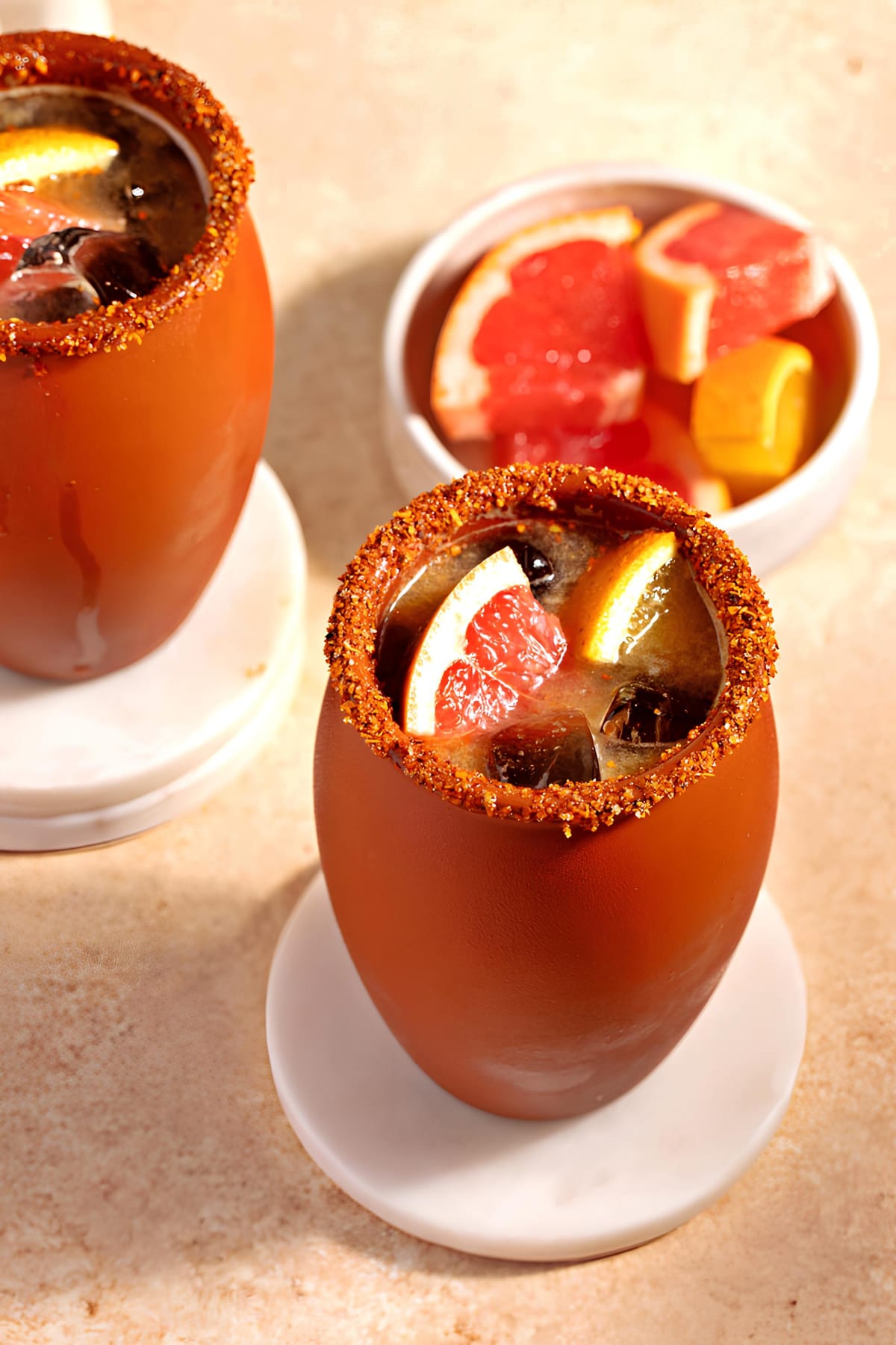 Cocktails served Cantarito mugs with tajin on rims garnished with slices of fresh graprfruit.