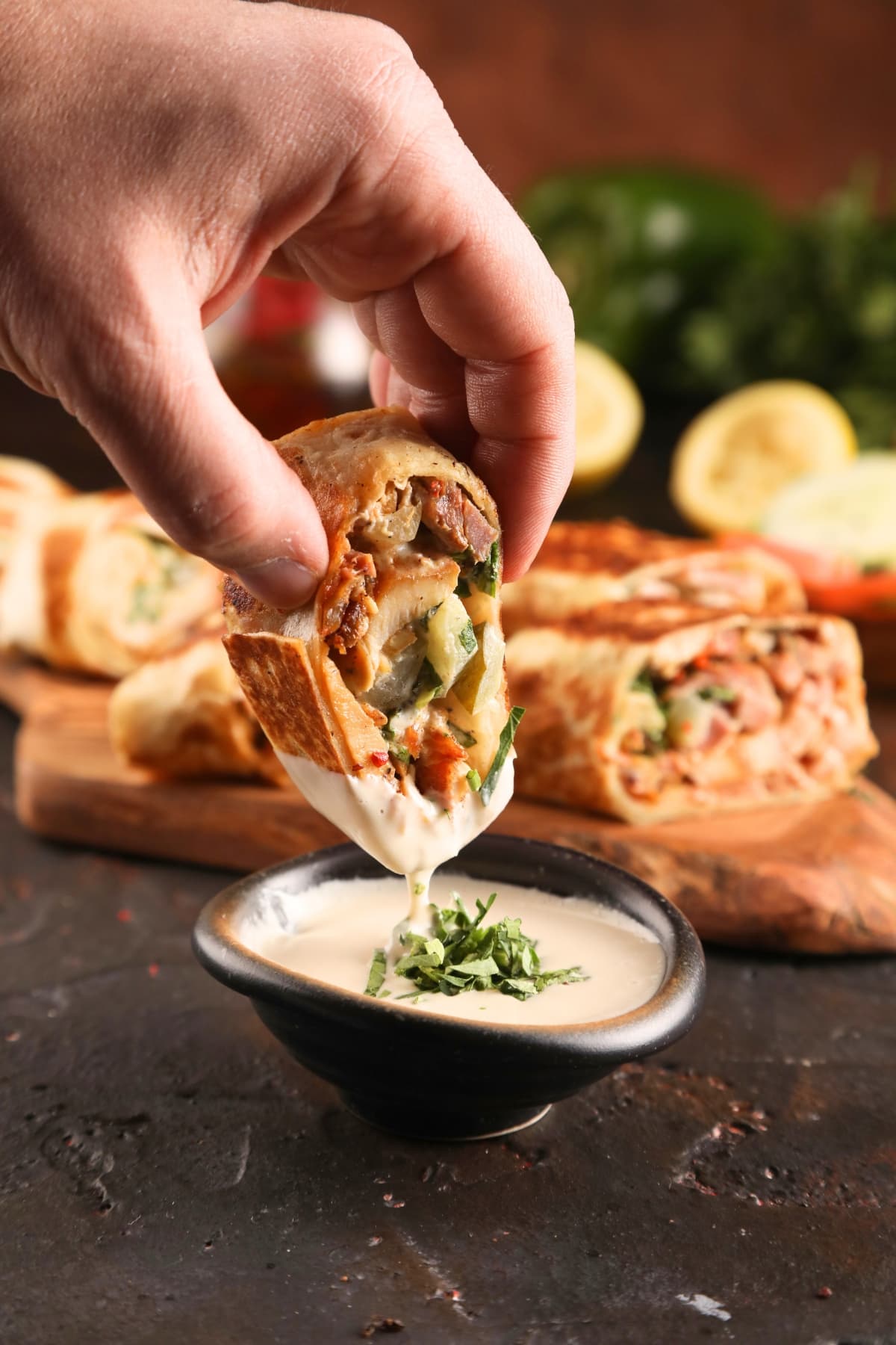 A person dipping a chicken shawarma into a bowl of sauce