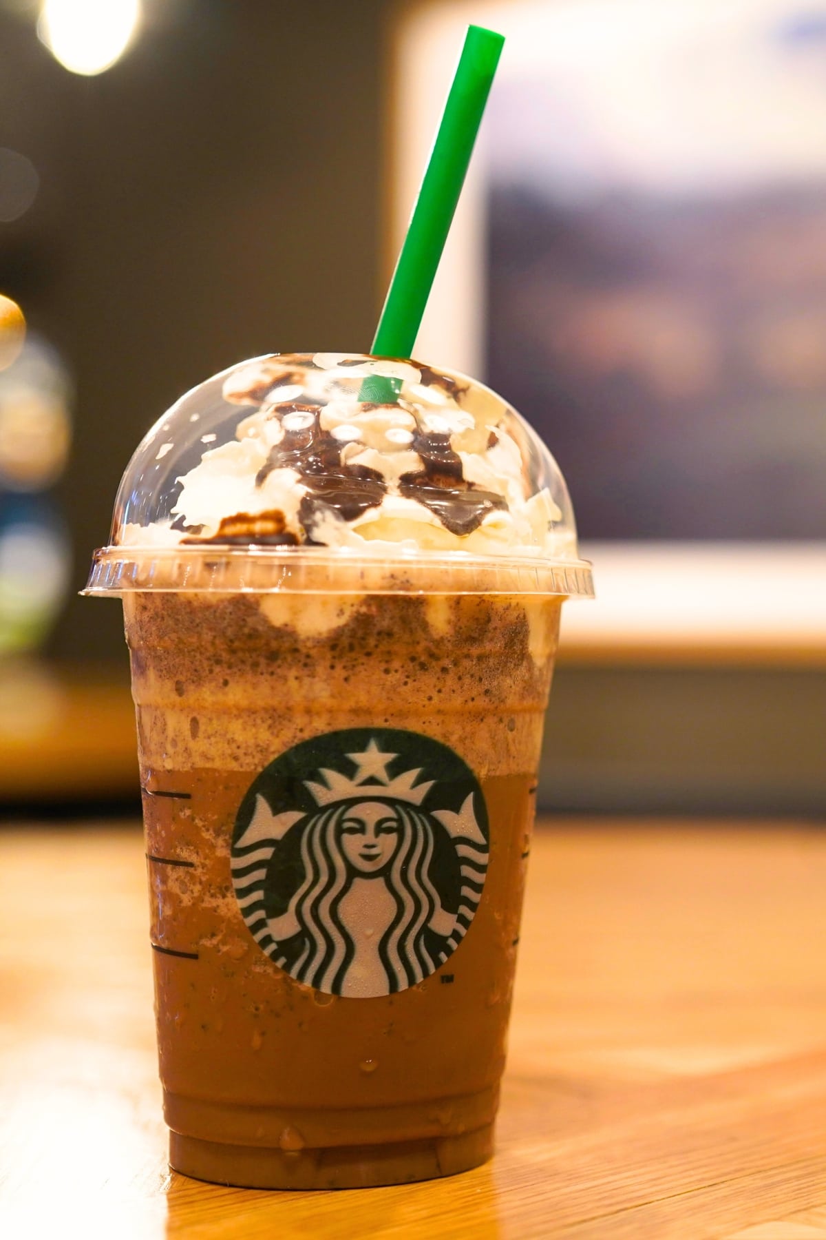 Chocolate frappe with green straw in wooden table.