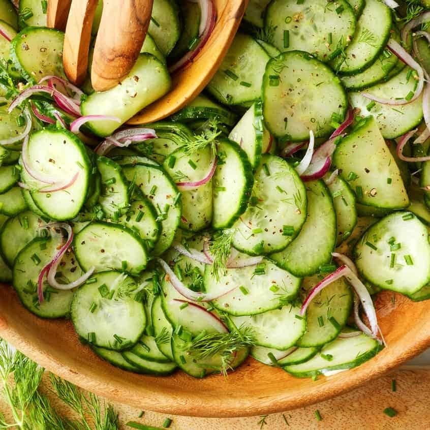 Cucumber salad on a wooden bowl with dill and sliced onions. 