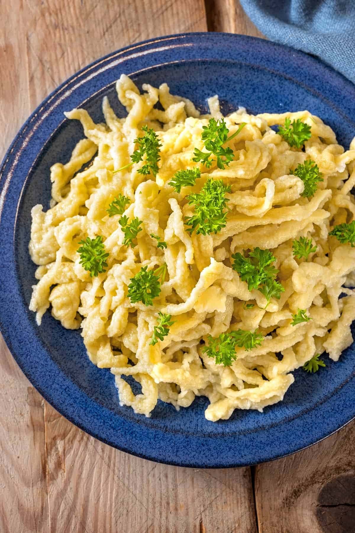 A serving of German Spaetzel on a blue plate garnished with chopped parsley. 