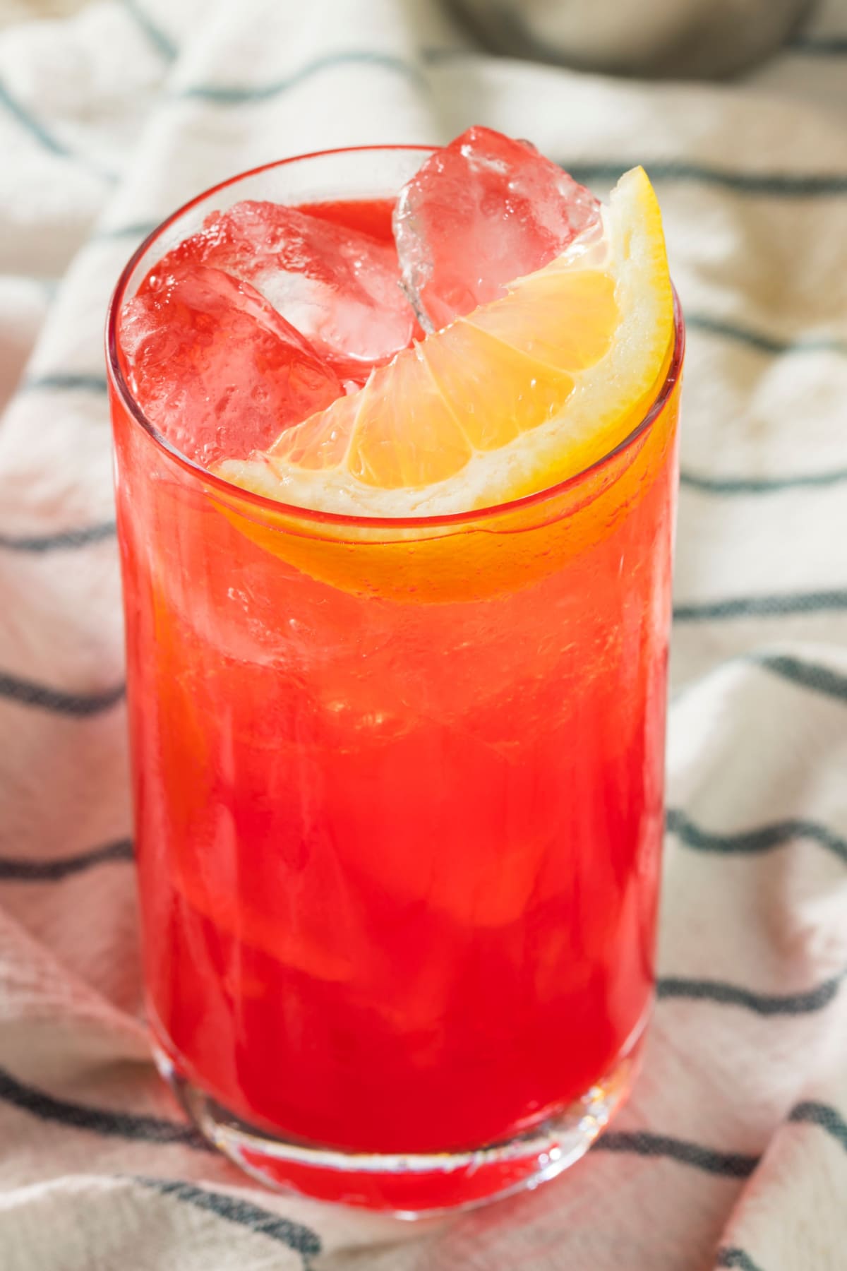 Top view of a glass of ice filled sloe gin fizz in a tall glass garnished with lemon slice. 