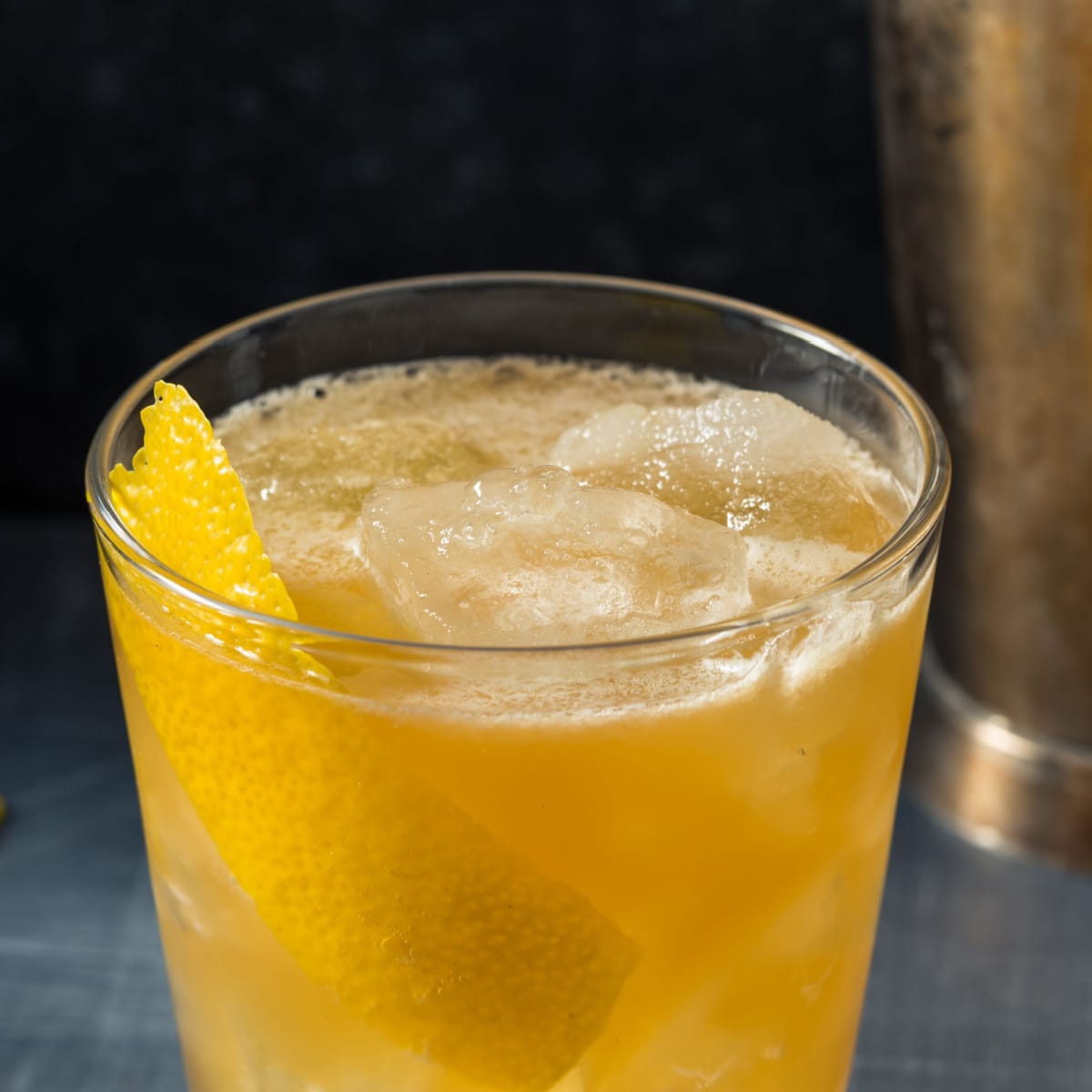 Ice cold gold rush cocktail on a glass garnished with lemon peel. 