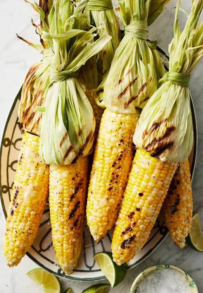Grilled corn with husk on plate. 