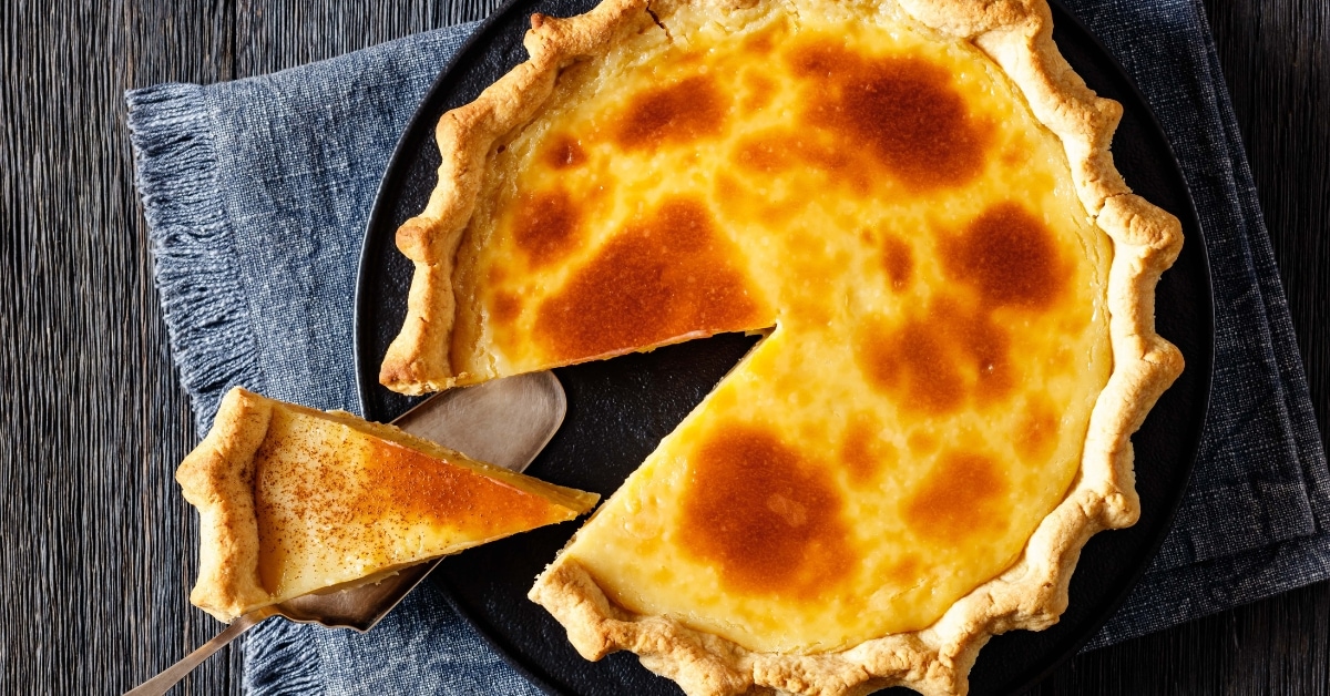 A slice of homemade sugar cream pie sits on top of a wooden table