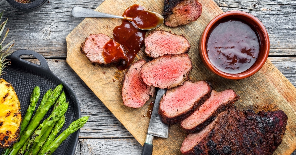 Barbecue dry aged wagyu tri tip steak with grilled pineapples and green asparagus on a wooden background