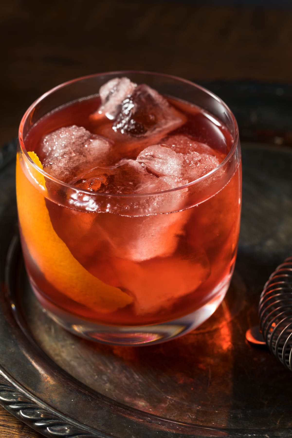 Boulevardier cocktail served on a glass filled with ice garnished with orange peel- close up. 