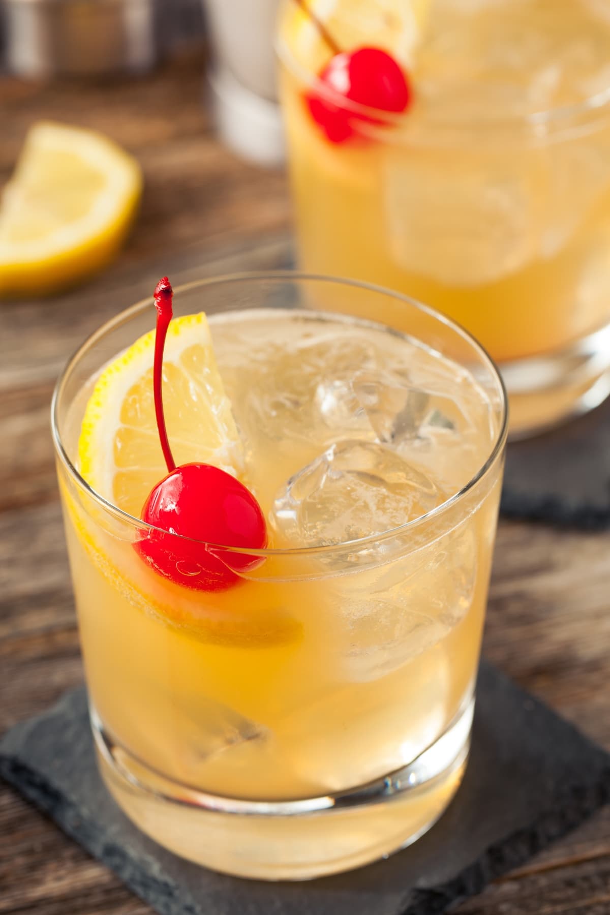 Whiskey sour cocktail served on a glass filled with ice garnished with lemon and cherry. 