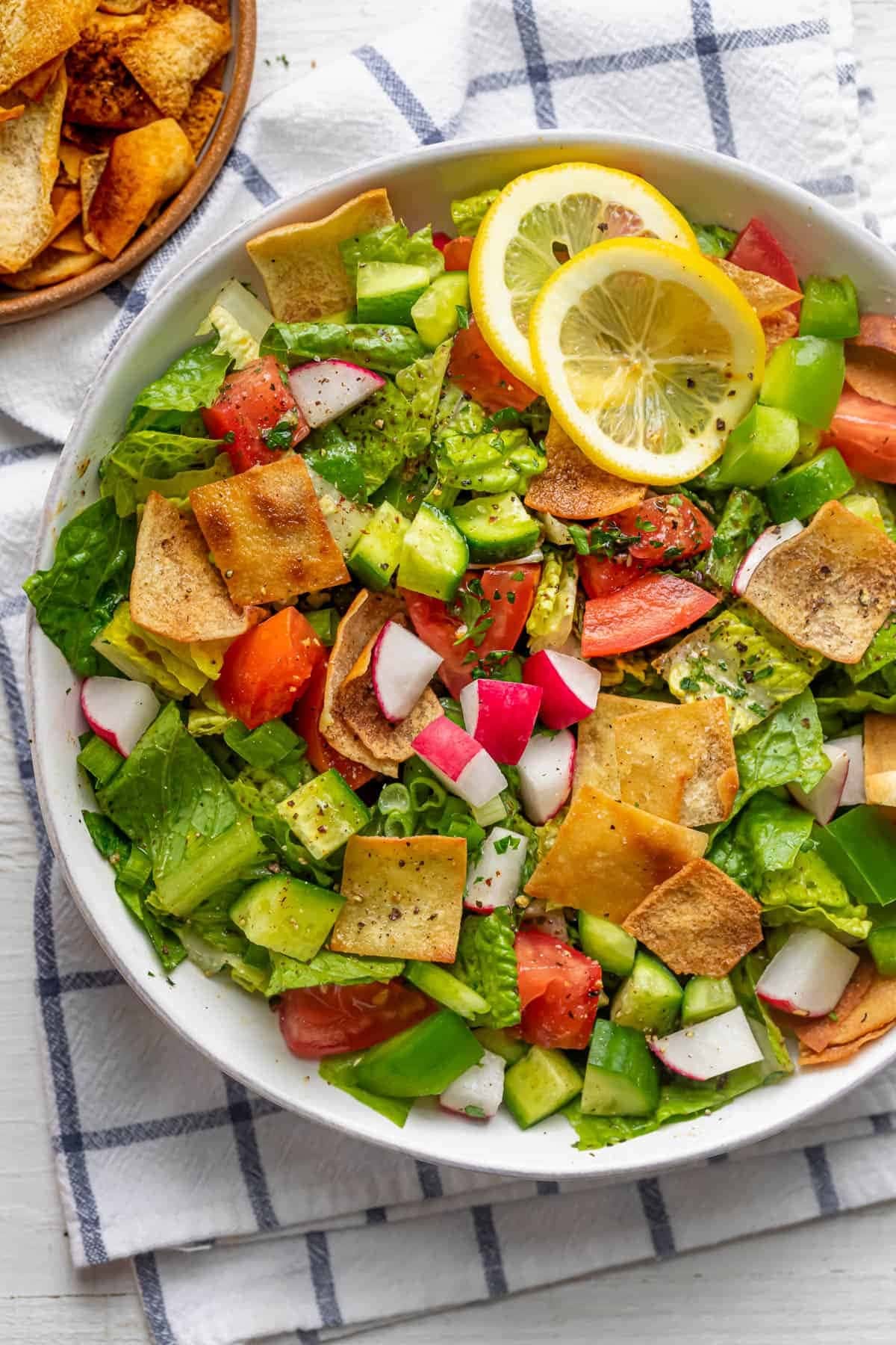 Salad on a white bowl made with lettuce, tomatoes, cucumbers, radishes and fried pieces of pita bread. 