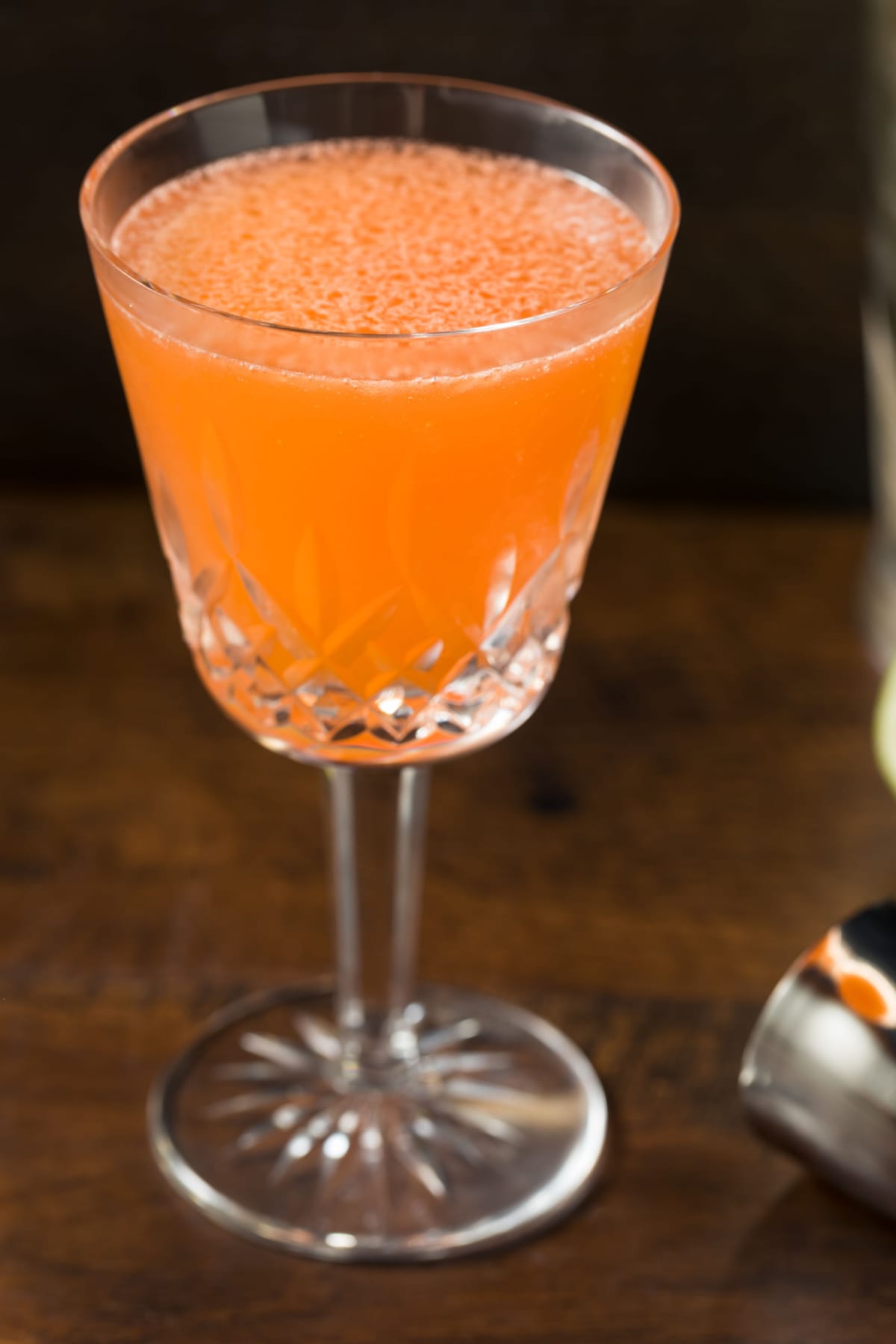 Orange cocktail served in a tall wine glass on top of a wooden table. 