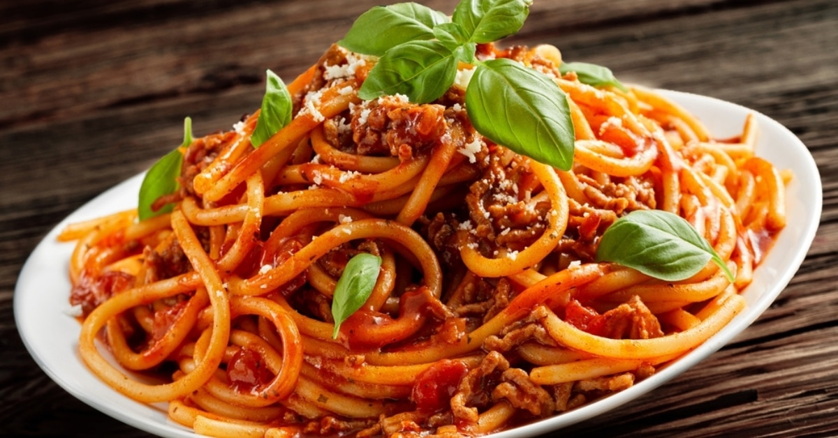 Serving of one pot spaghetti on a white plate garnished with basil leaves and parmesan cheese.