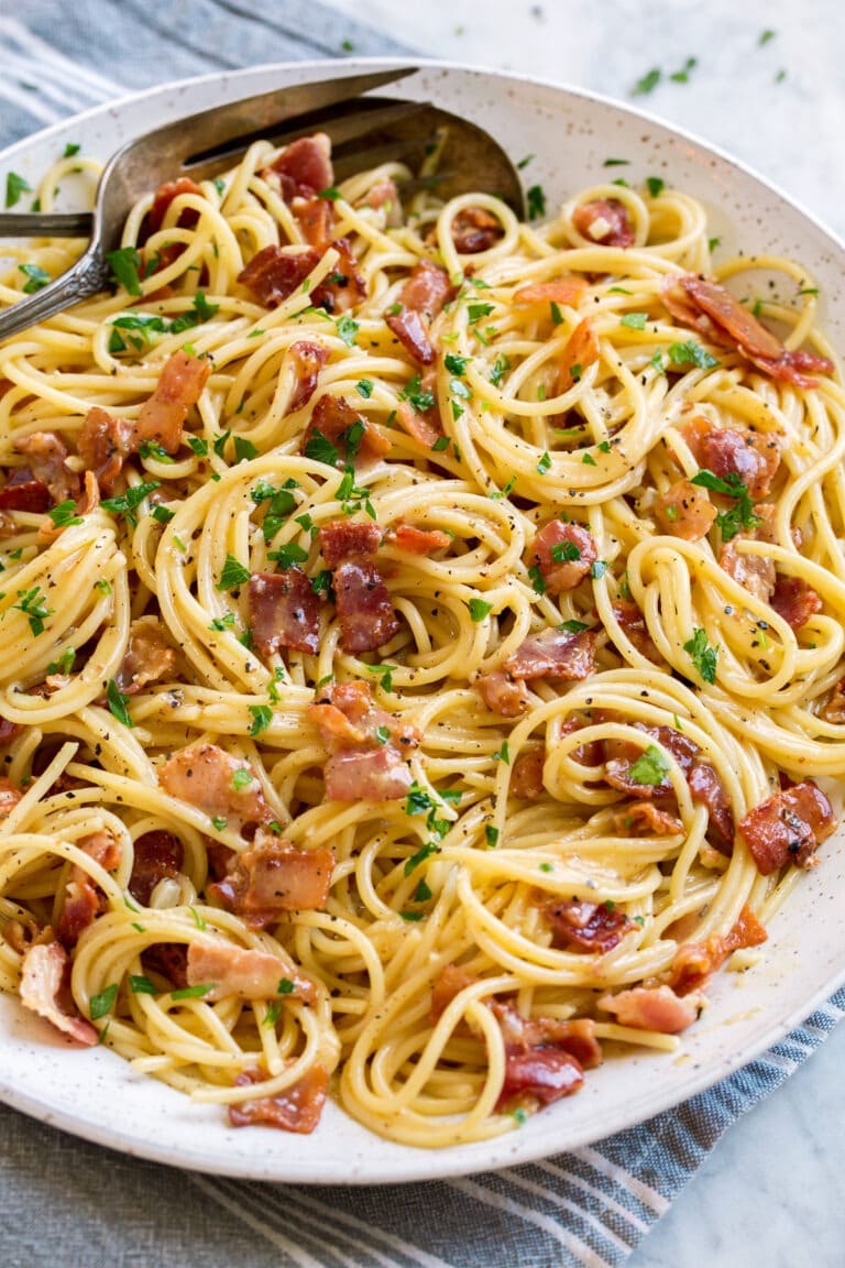 Carbonara pasta with bacon bits garnished with chopped parsley leaves.