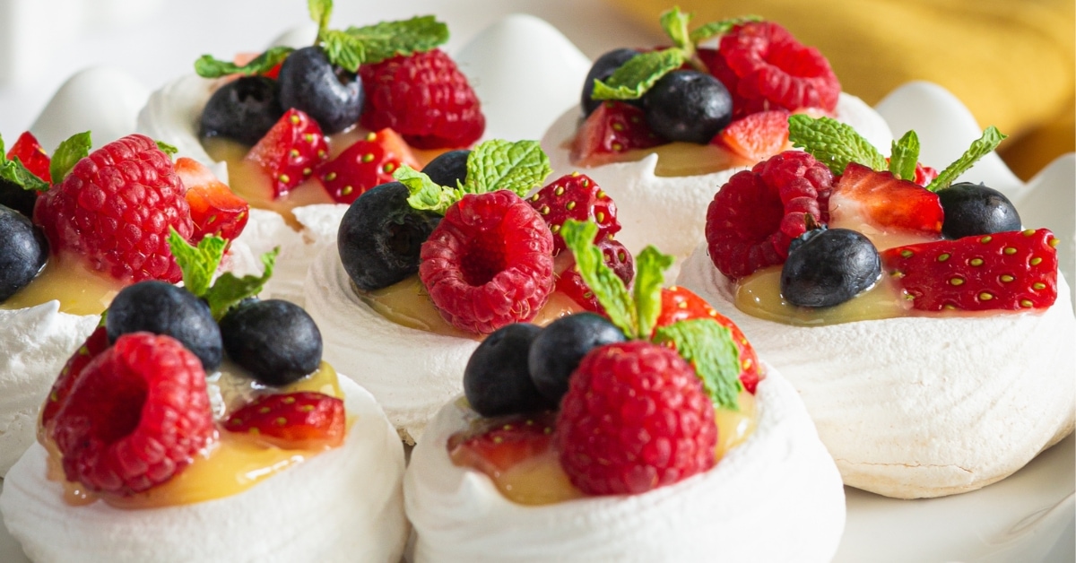 Pavlova topped with custard and berries served on a cake tray.