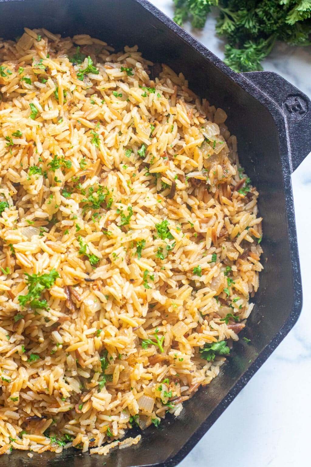 Rice pilaf in a stoneware pan made with mix of rice and orzo with spices, herbs, sauteed onions, and garlic.