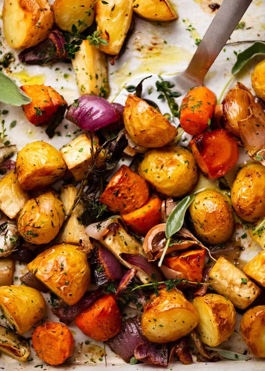 Roasted potatoes, onions, tomatoes with rosemary leaves on a sheet pan with parchment paper lining.