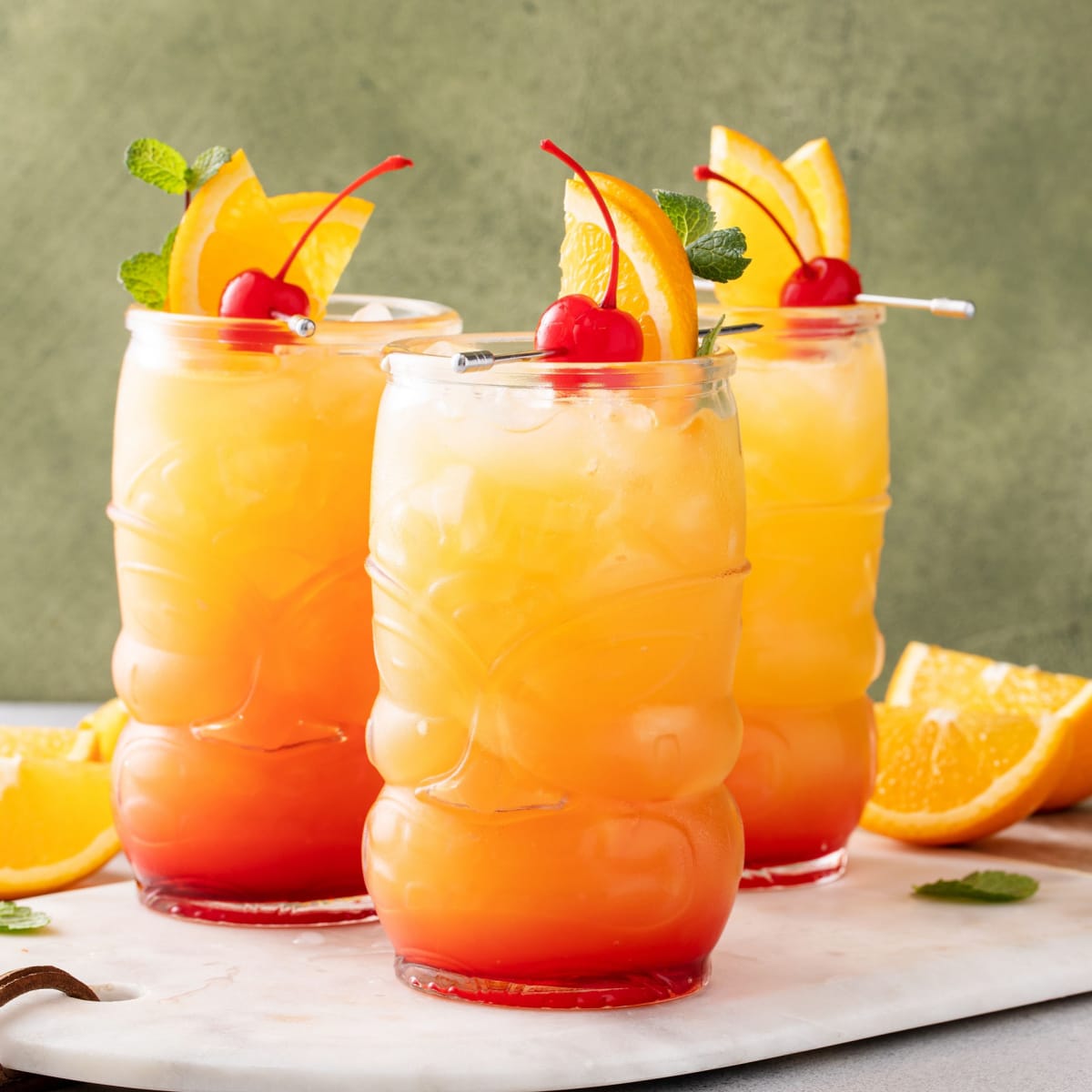 Three glasses of rum punch garnished with cherries and orange slices. 