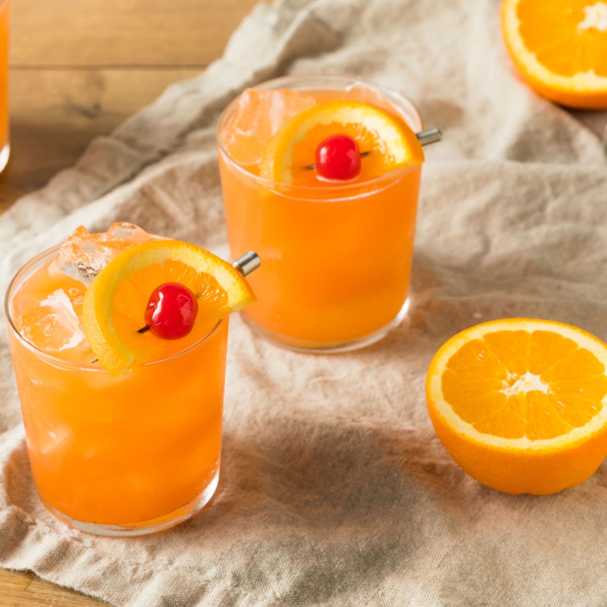 Ice filled  rum swizzle cocktail served on glasses garnished with orange peel and cherry. 