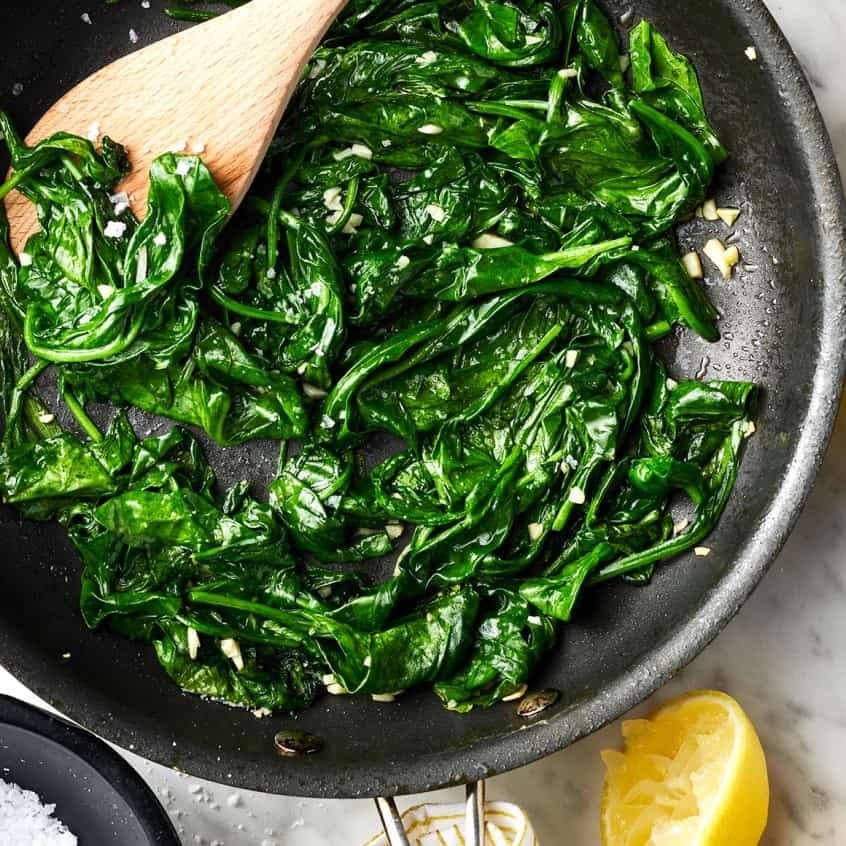 Wooden spoon tossing a  sauteed Spinach on a pan.