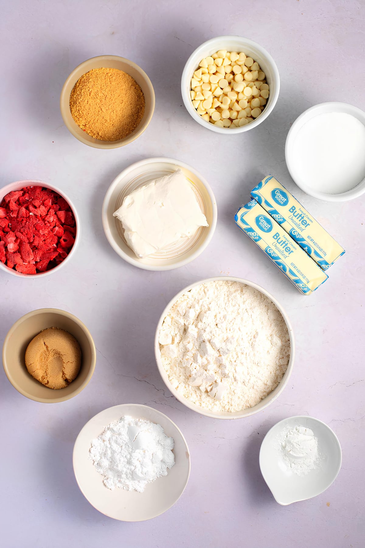 Portions of white chocolate chips, graham crackers, strawberry, butter, powdered sugar, cinnamon powder, flour on a white bowl. 