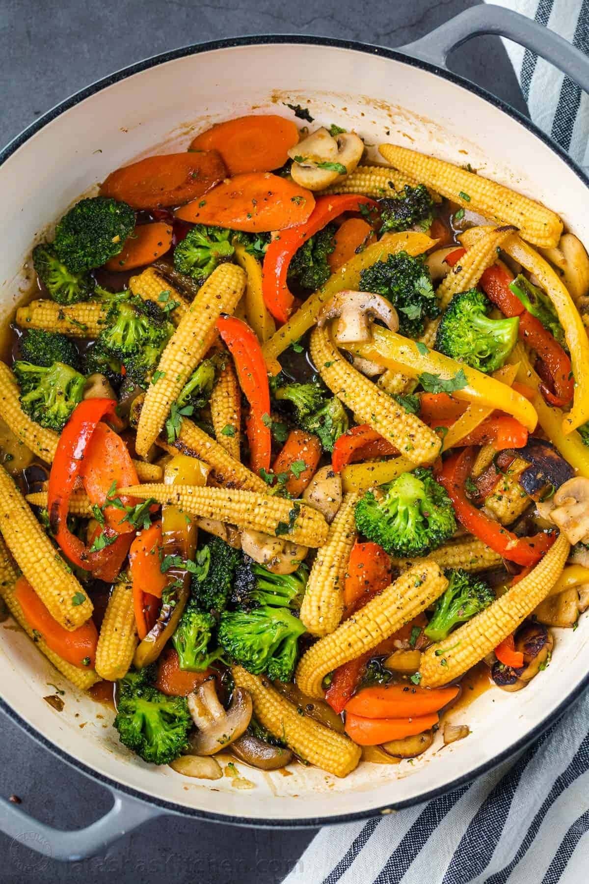 Baby corn spears, mushrooms, red pepper and broccoli stir fried on a white pan.