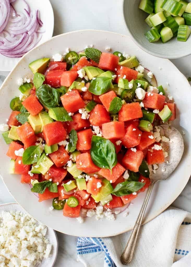 Salad on a plate made with sliced watermelon, feta cheese, avocado, mint and dressing. 