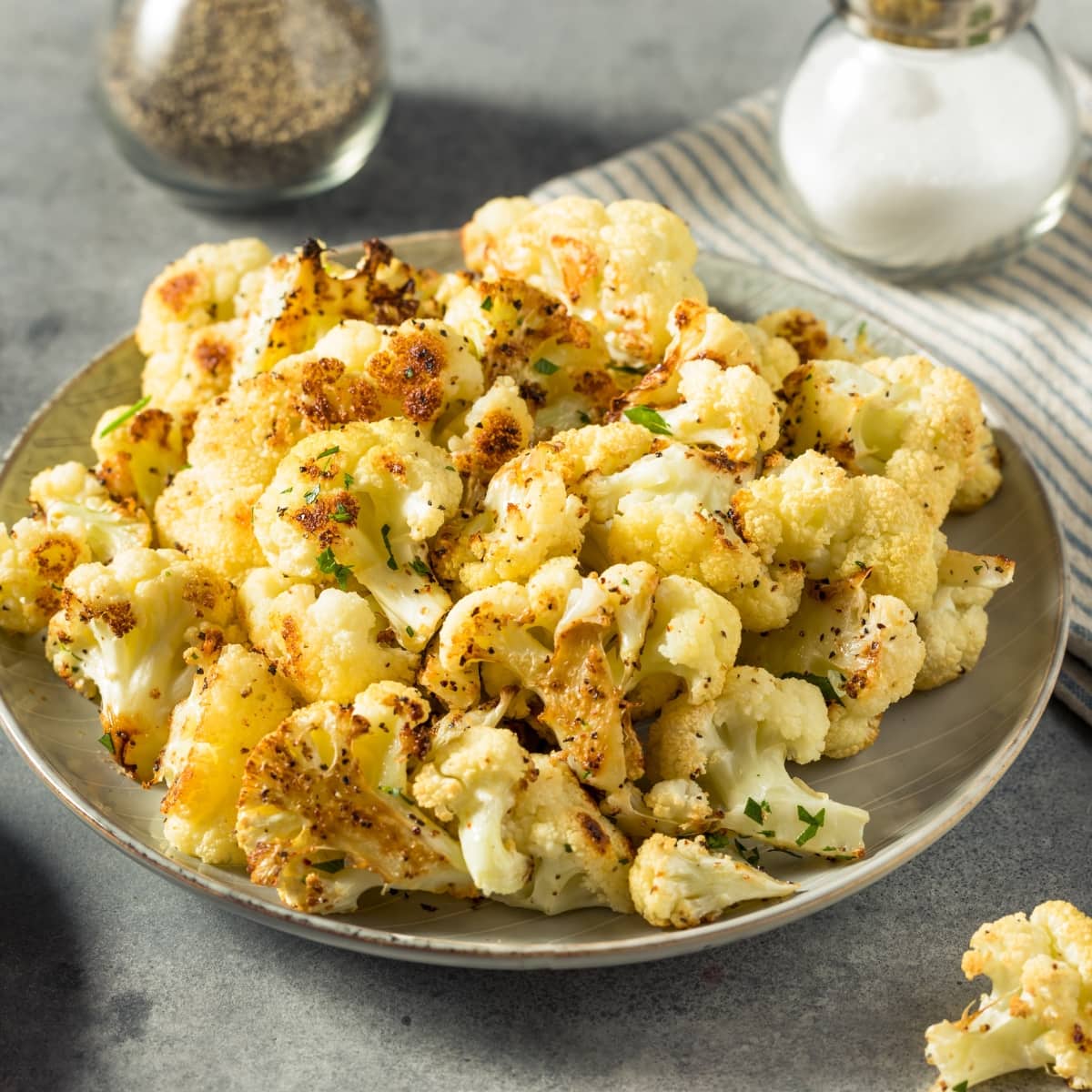 Serving of bunch of roasted cauliflower on a grate plate seasoned with pepper and paprika.