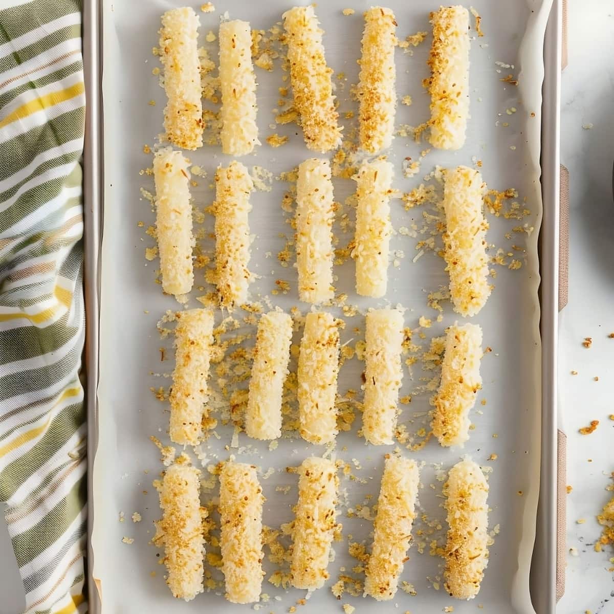 Coated mozzarella sticks with egg in a baking sheet, top view