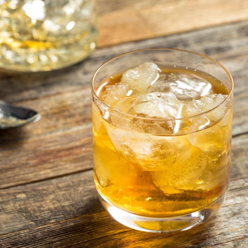 Godfather cocktail in an old fashioned glass filled with ice on top of a wooden table. 