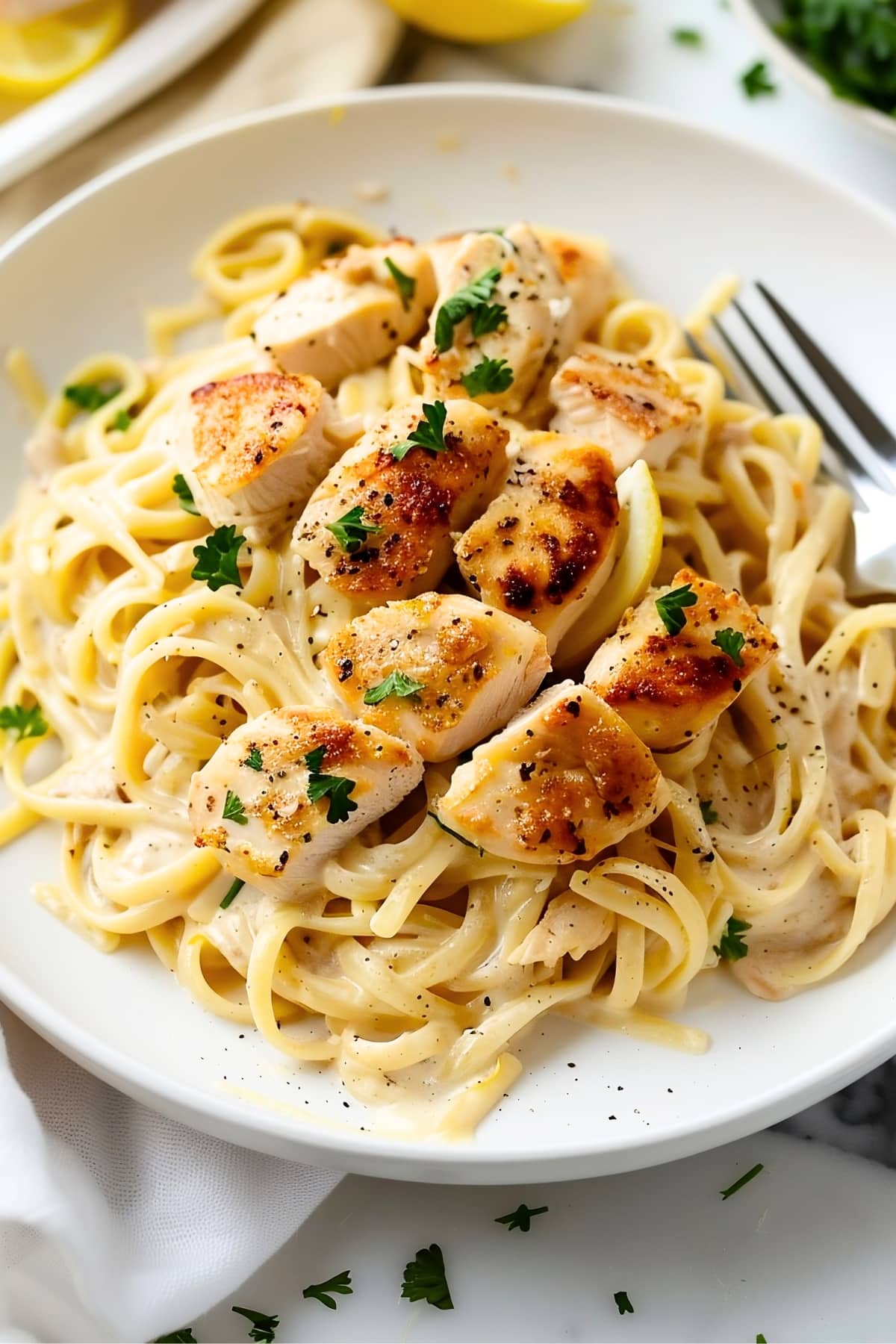 Creamy lemon chicken pasta garnished parsley in a white plate on a white marble table