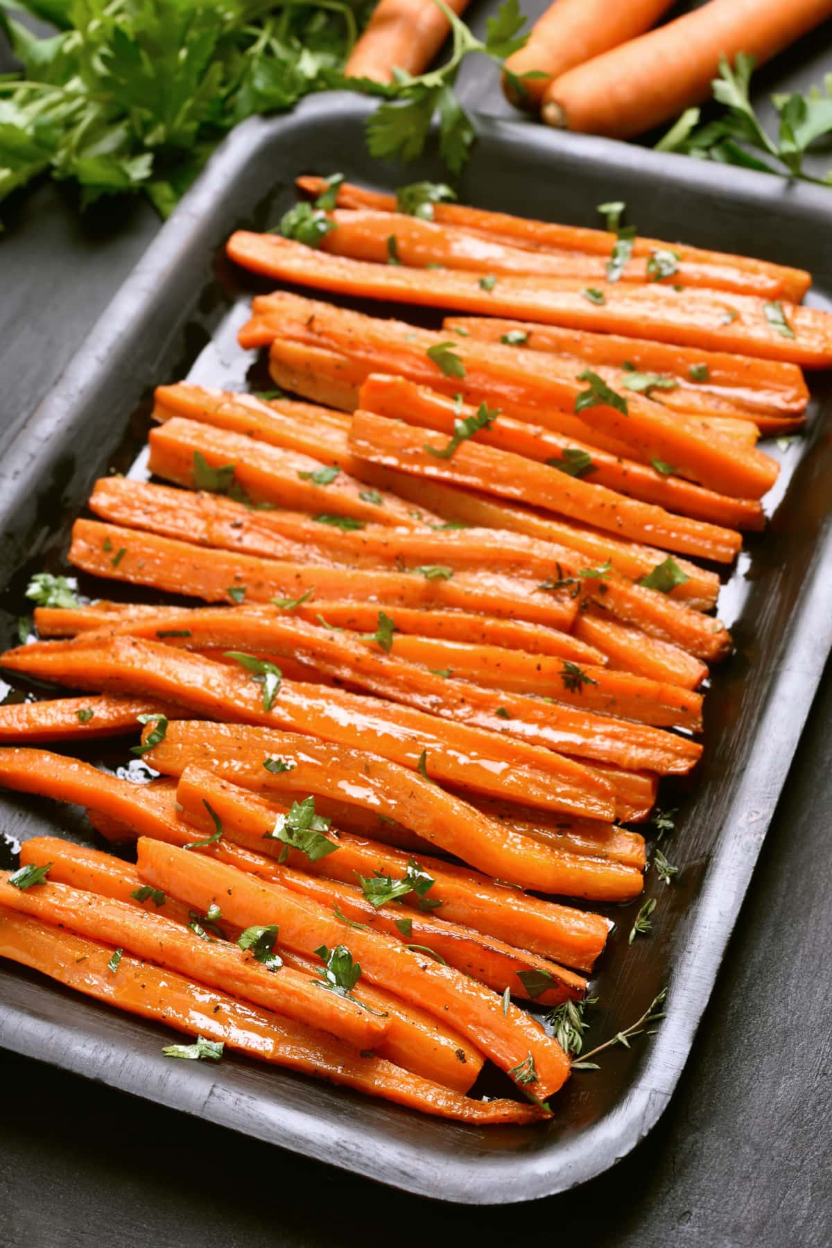 Honey roasted carrots on a baking pan garnished with chopped parsley. 