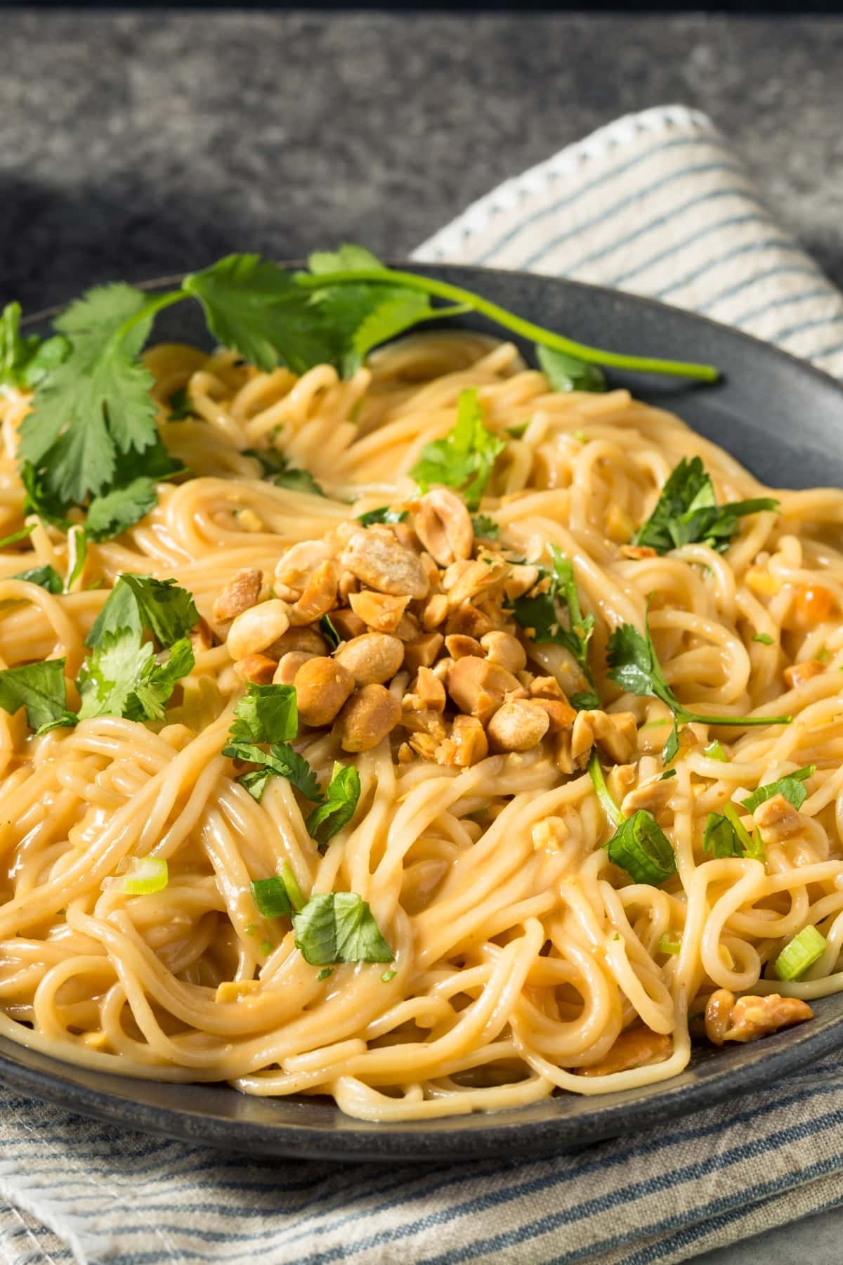 Peanut noodles on a black plate garnished with nuts and cilantro leaves.